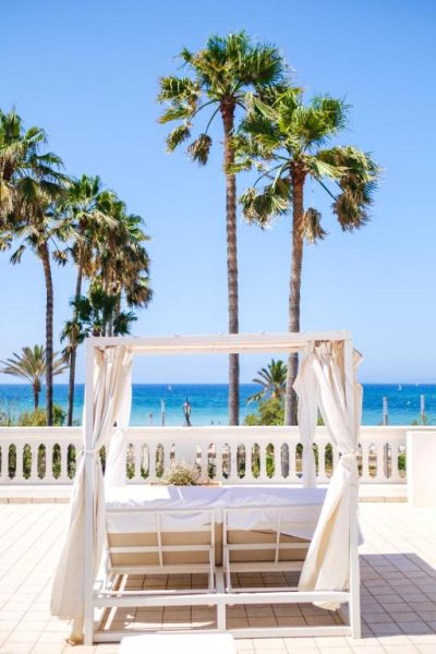 Cama balinesa con dosel blanco en la terraza del Hotel Ciutat Jardi con vistas al mar y palmeras
