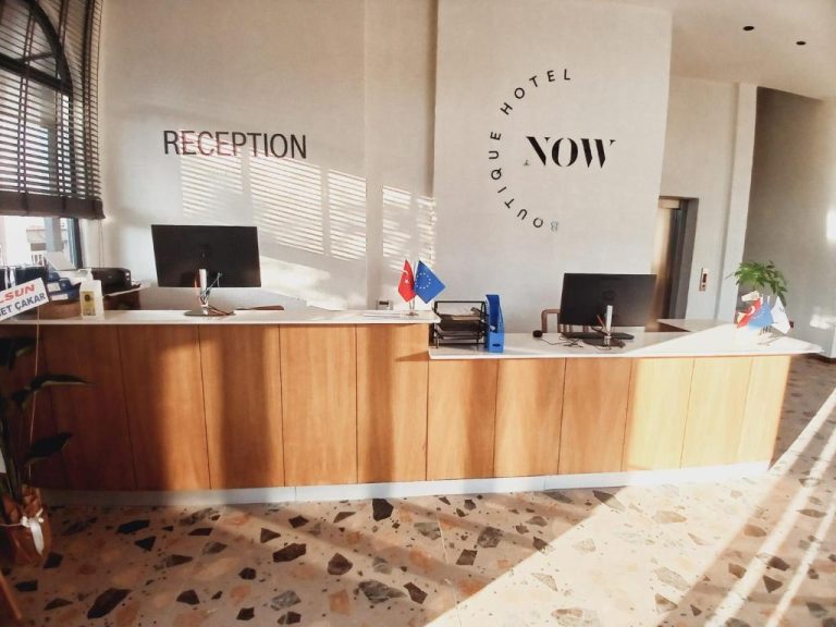 Recepción moderna del Now Boutique Hotel con mostrador de madera y banderas de Turquía y Europa