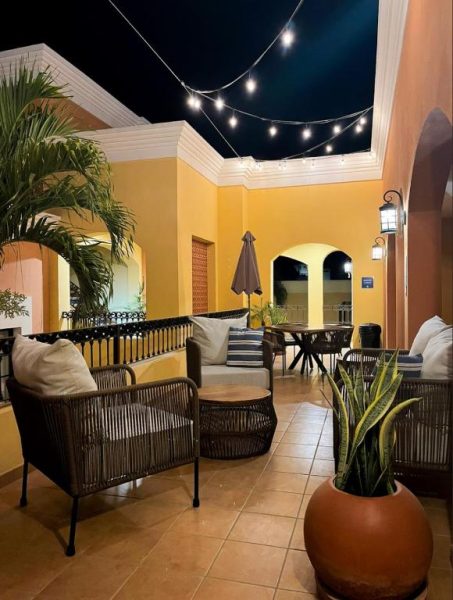 Terraza exterior del Hotel Colli con mobiliario de ratán, luces colgantes y paredes amarillas por la noche