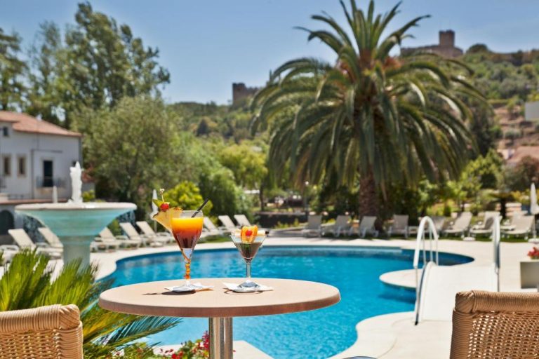 Piscina exterior con cocteles tropicales y palmeras del Hotel Dos Templarios en un día soleado