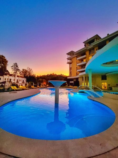 Piscina exterior iluminada con fuente central del Hotel Dos Templarios al atardecer