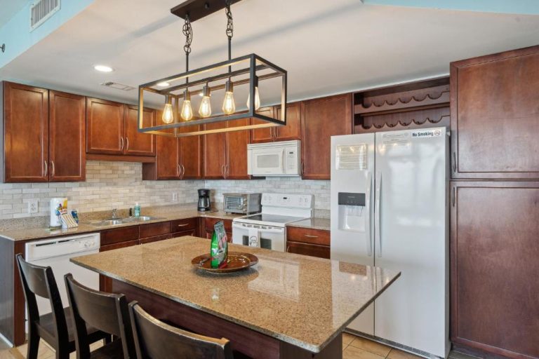 Cocina moderna con isla de granito, armarios de madera y electrodomésticos blancos en Gulf View Condo