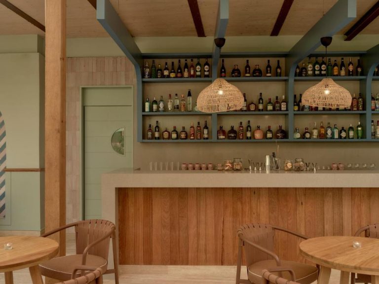 Bar interior con estantes de licores y mobiliario de madera natural en Kimpton Las Mercedes by IHG