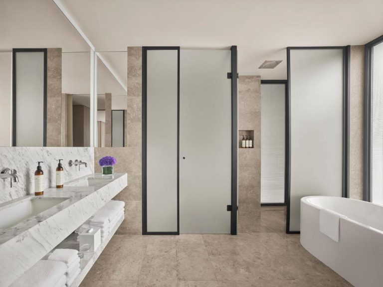 Baño de lujo con bañera exenta, encimera de mármol y ducha independiente en The Bodrum EDITION