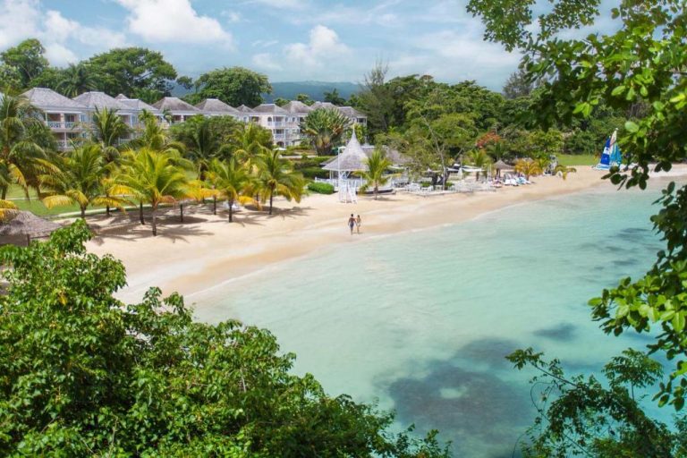 Playa privada de arena blanca con aguas turquesas y palmeras del resort Couples Sans Souci en Jamaica