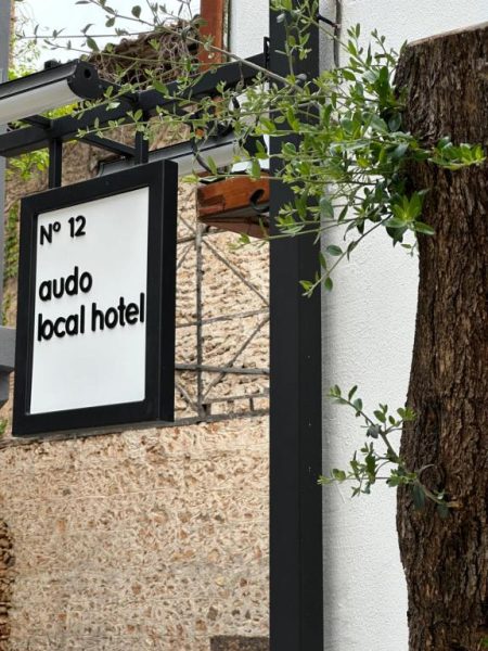Cartel de entrada del Audo Local Hotel número 12 en fachada de piedra con vegetación