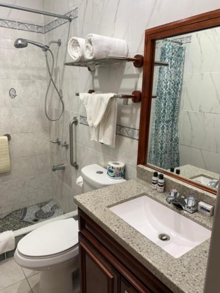 Baño completo con ducha, lavabo de granito y toallas blancas en el Rayon Hotel