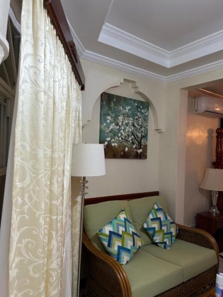 Salón con sofá de ratán y cojines coloridos en Rayon Hotel, decoración colonial con arco y cuadro floral