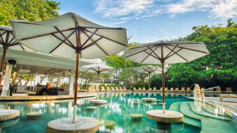 Piscina tropical con sombrillas sobre el agua en Bali Garden Beach Resort, rodeada de jardines