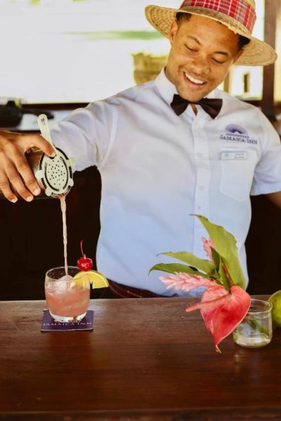 Bartender del Jamaica Inn preparando un cóctel tropical con frutas frescas en la barra del hotel