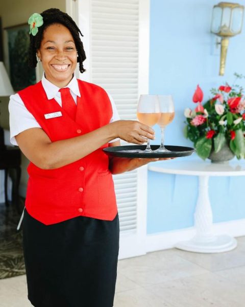 Camarera sonriente del Jamaica Inn ofreciendo copas de vino rosado en bandeja de bienvenida