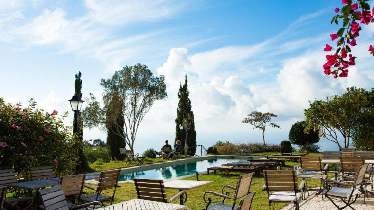 Piscina exterior con tumbonas y jardín con vistas al mar del Hotel Atrio en día soleado
