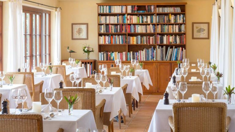 Restaurante del Hotel Atrio con mesas vestidas en blanco y gran biblioteca de fondo