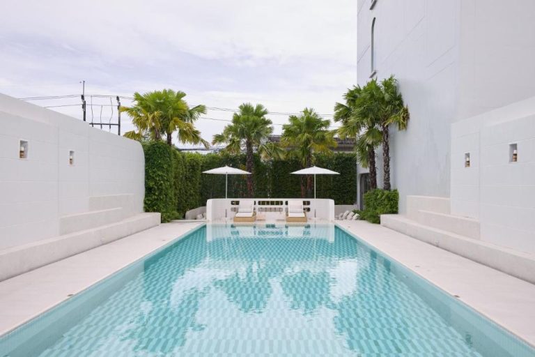 Piscina exterior con tumbonas y palmeras tropicales del hotel Arco Phuket Town en Tailandia