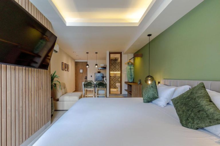 Habitación con cama doble, pared verde y cocina americana en De la Cruz Studio Apartments