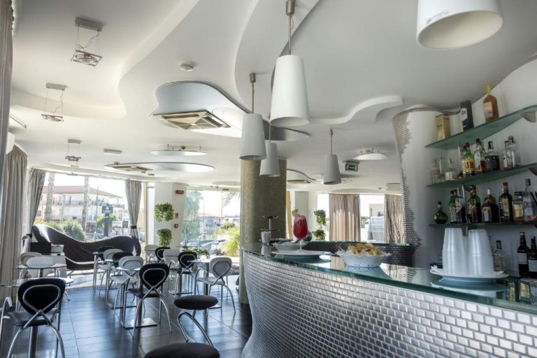 Bar y salón moderno del Hotel Kore con barra de cristal, taburetes y estantería de bebidas