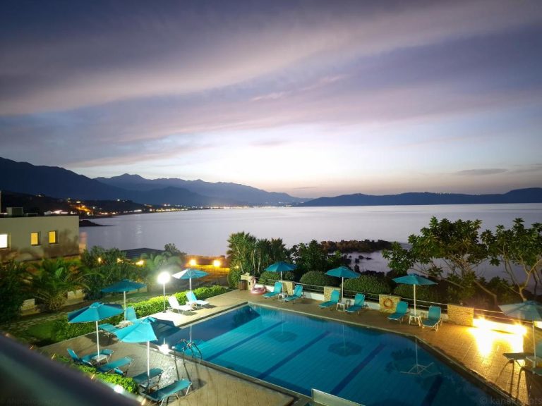 Piscina exterior iluminada con vistas al mar y montañas al atardecer en Kanakis Blue Beach Apartments