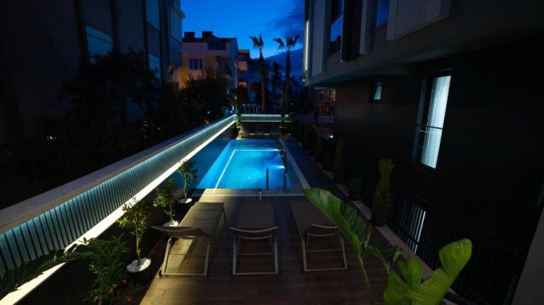 Piscina exterior iluminada de noche en el Stile Suite Marine Hotel con terraza y tumbonas