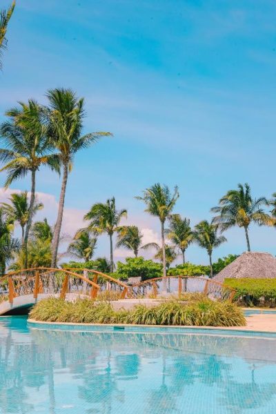 Piscina exterior con puente de madera y palmeras tropicales en Fiesta Resort All Inclusive Costa Rica