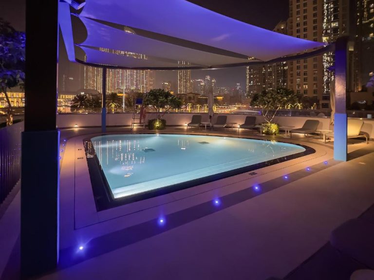 Piscina iluminada de noche con vistas al skyline de Dubái en apartamento de lujo cerca de Dubai Mall