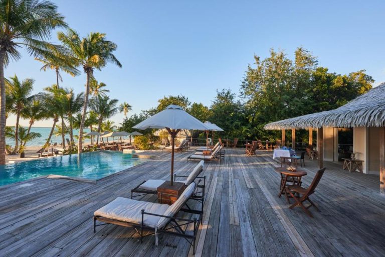 Terraza de madera con piscina infinita y tumbonas junto a la playa en Tiamo Resort Bahamas