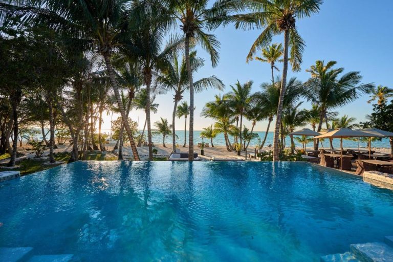 Piscina infinita del Tiamo Resort con vistas al mar y palmeras tropicales en primer plano