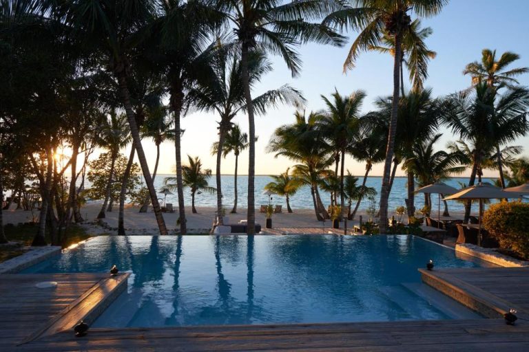 Piscina infinita del Tiamo Resort con vistas a la playa y palmeras tropicales al atardecer