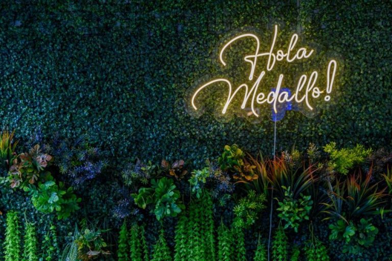 Mural de plantas naturales con letrero de neón que dice Hola Medallo en el Hotel Hola Medellín