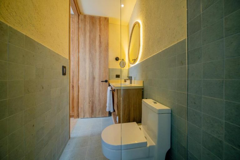 Baño moderno del Moabi Hotel con azulejos verdes, inodoro blanco, lavabo y espejo oval iluminado