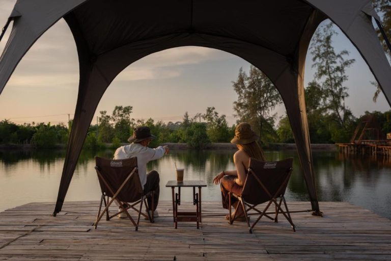 Pareja relajándose en terraza sobre el lago al atardecer en Camp Cayla Coasta con carpa y sillas de camping