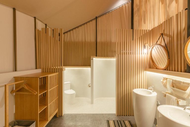 Baño moderno con paredes de listones de madera, lavabos blancos y tocador iluminado en Camp Cayla Coasta