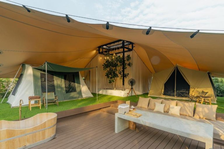 Zona de glamping de lujo con tiendas safari, sofá y bañera de madera en Camp Cayla COASTA
