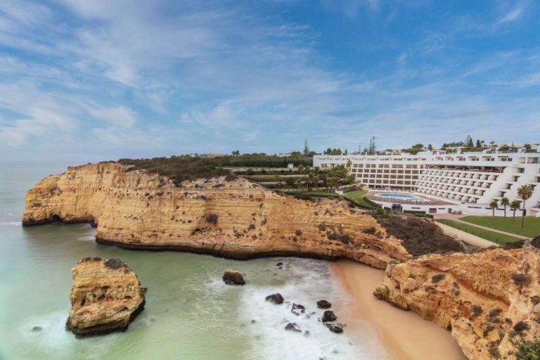 Vista aérea del Tivoli Carvoeiro con impresionantes acantilados dorados, playa y piscina exterior en el Algarve