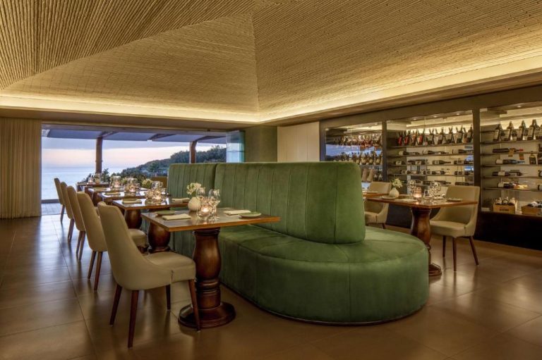 Elegante restaurante del Tivoli Carvoeiro con sofá verde, bodega y vistas al mar al atardecer