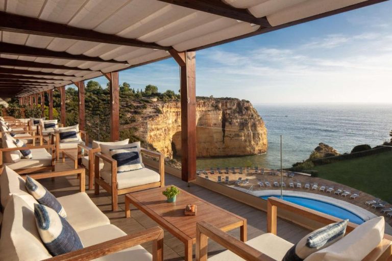 Terraza con sofás y piscina exterior del Tivoli Carvoeiro con vistas al acantilado y mar