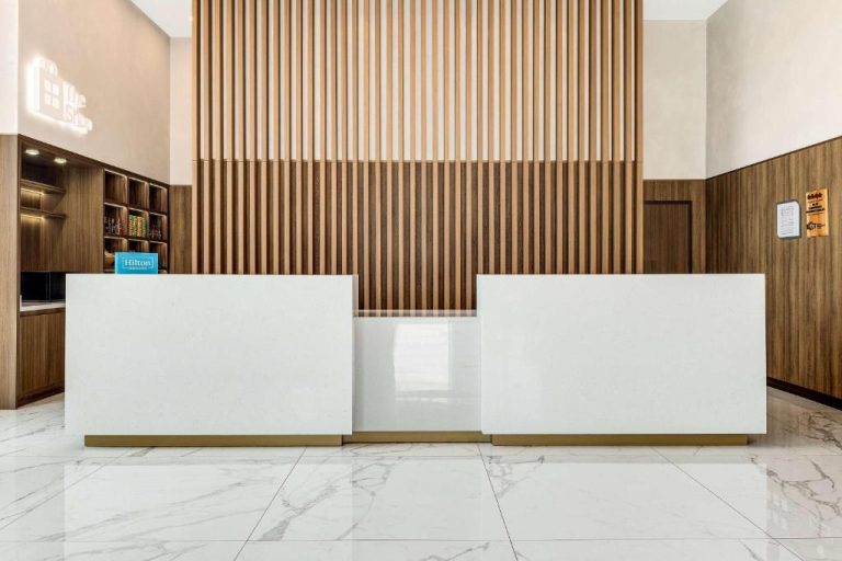 Recepción moderna con mostrador blanco y revestimiento de madera en Hilton Garden Inn San José Airport City Mall
