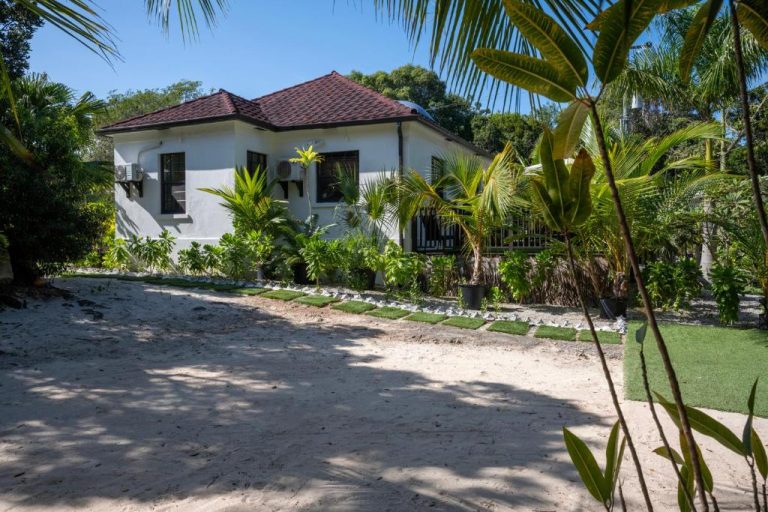 Fachada exterior de The Pilot House rodeada de jardín tropical con palmeras y arena blanca