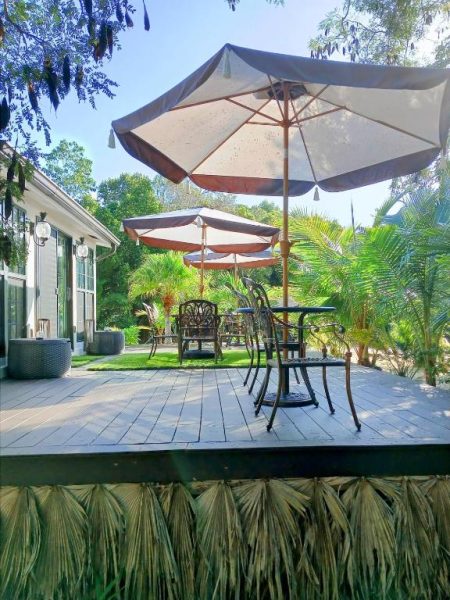 Terraza de madera con mesas, sillas y sombrillas en The Pilot House rodeada de vegetación tropical
