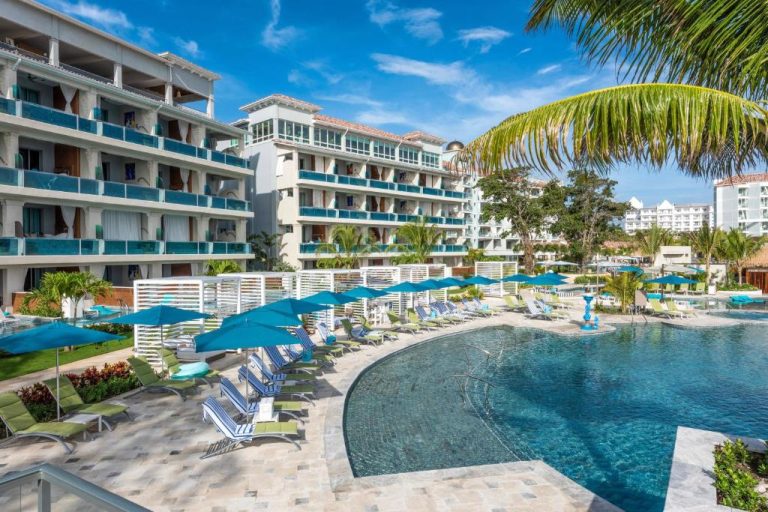 Piscina exterior con tumbonas y sombrillas azules en Sandals Dunns River, resort adults only en Jamaica