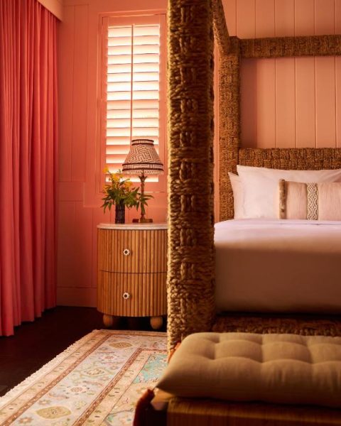 Habitación con cama de dosel en rattan y decoración en tonos coral del Coral Sands Inn & Cottages