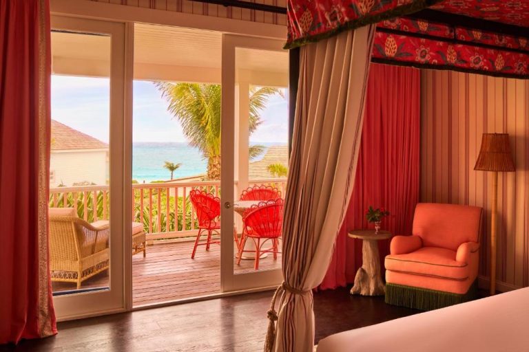 Habitación con dosel rojo y terraza con vistas al mar turquesa en Coral Sands Inn & Cottages