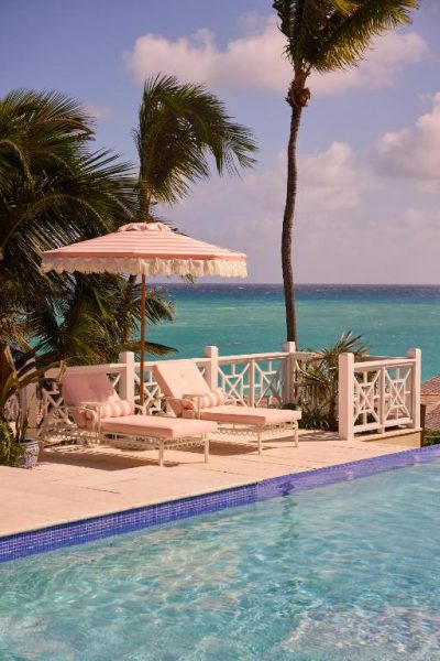 Piscina infinita con tumbonas rosas y sombrilla frente al mar turquesa en Coral Sands Inn & Cottages