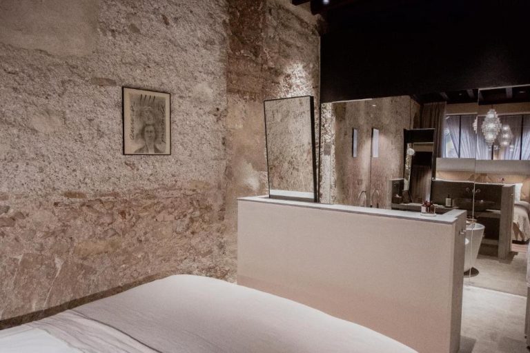 Habitación de lujo con baño integrado y paredes de piedra histórica en Nobis Hotel Palma