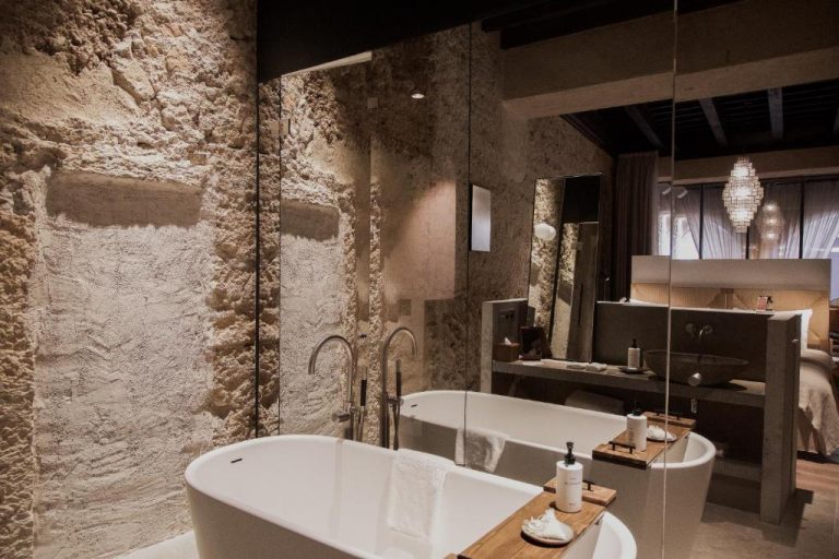 Lujoso baño con bañera exenta y pared de piedra natural en Nobis Hotel Palma Design Hotels
