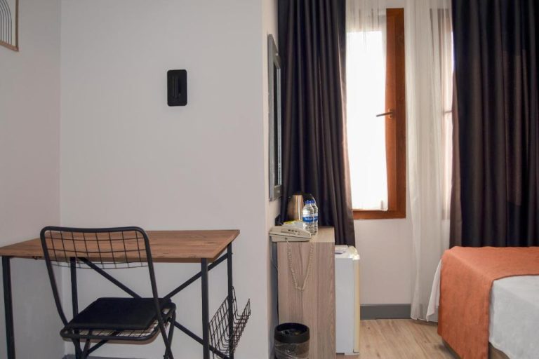 Habitación del Akkan Hotel con escritorio de madera, silla industrial y cama con colcha naranja