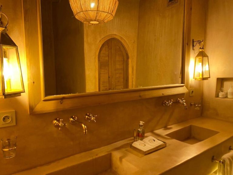 Baño rústico con lavabo de cemento y lámparas de farol doradas en Casa Abracadabra