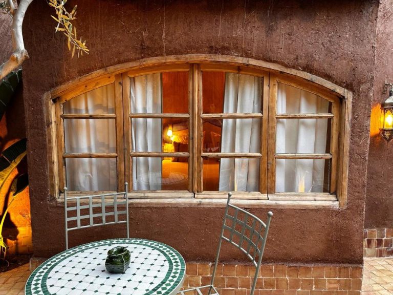 Patio exterior con mesa de mosaico y ventana arqueada de madera en Casa Abracadabra