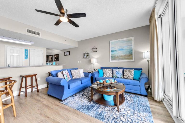 Sala de estar con sofás azules y decoración costera en apartamento con vistas al mar en Panama City Beach