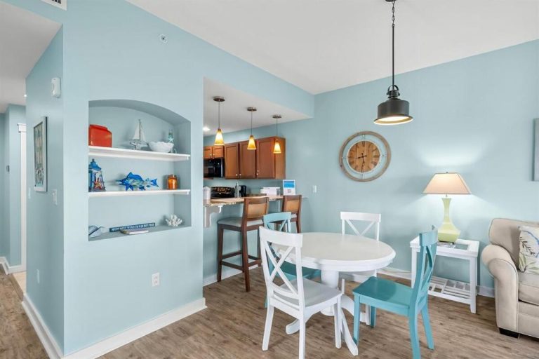 Comedor con mesa blanca y sillas turquesa junto a cocina abierta en Origin 1227 Beachy Dreams