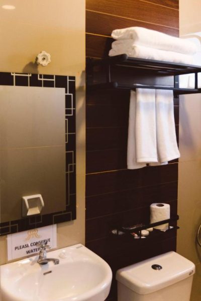 Baño moderno con lavabo, espejo y toallas blancas en Surigao Royal Regency Suites